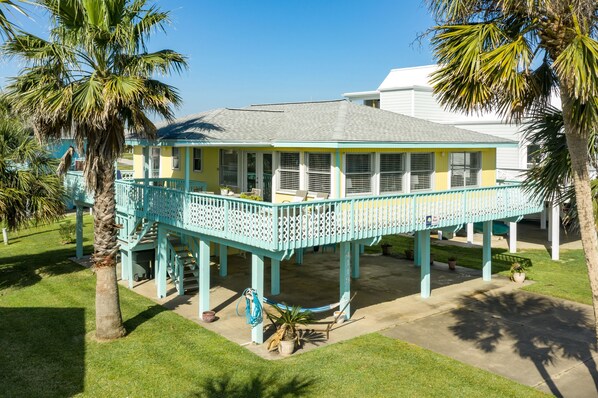 A two-story house with a balcony, surrounded by palm trees and a well-maintained lawn. - Updated Beachside Home w/ Fully Equipped Kitchen, Large Deck+Patio, Dog Friendly (Galveston)