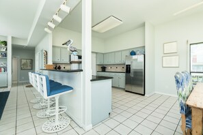 Une cuisine moderne avec des meubles de couleur bleu clair, un îlot central doté de tabourets de bar, des appareils électroménagers en acier inoxydable et une vue sur la ville grâce à de grandes fenêtres.