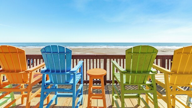 A wooden deck with colorful Adirondack chairs overlooking a beach. - Panoramic View Beachfront Home - Easy Beach Access, Outside Shower, Dog Friendly (Galveston)