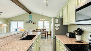 A kitchen with granite countertops, a refrigerator, a stove, and a dining area with chairs and a table. - Panoramic View Beachfront Home - Easy Beach Access, Outside Shower, Dog Friendly (Galveston)