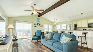A spacious living room with a blue sofa, wooden flooring, and a ceiling fan. - Panoramic View Beachfront Home - Easy Beach Access, Outside Shower, Dog Friendly (Galveston)
