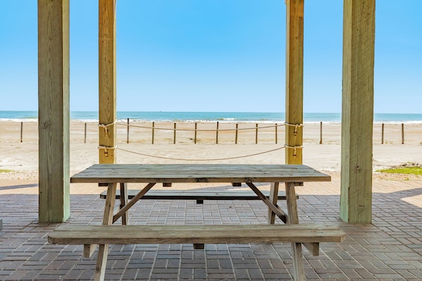 Une table de pique-nique en bois, avec des bancs, entourée d’une barrière faite de cordes, et offrant une vue sur la plage.