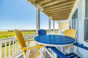 A covered outdoor seating area with a round table and two chairs, overlooking a grassy area with a view of the ocean.