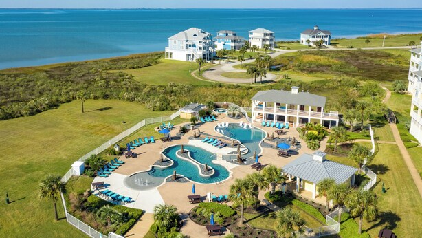 Vista aérea de um resort com uma piscina grande, várias alas para hóspedes e vista para o oceano.