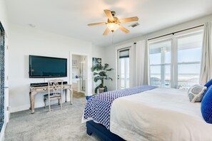 A bedroom with a bed, a desk, a television, and a large window with curtains.