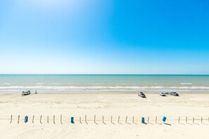 Una spiaggia con una riva sabbiosa, una recinzione di legno e diversi veicoli parcheggiati vicino all'acqua.