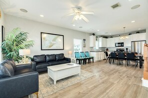 A modern living room with a black leather sofa, a white coffee table, and a dining area with chairs and a table.