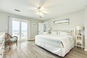 Un dormitorio con cama, una silla, una mesita de noche, ventilador de techo y vistas a través de una puerta.