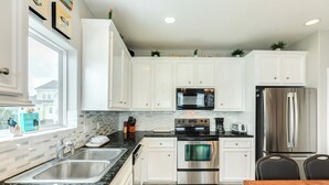 Una cocina con armarios blancos, electrodomésticos de acero inoxidable, encimera de granito y ventana con vistas a casas.