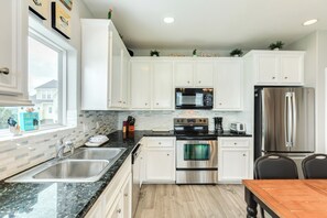 Una cocina con armarios blancos, electrodomésticos de acero inoxidable, encimera de granito y ventana con vistas a casas.