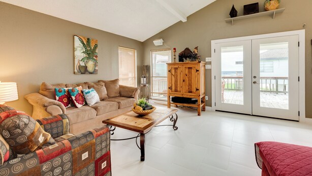 A living room with a beige sofa, patterned armchair, wooden coffee table, and a red ottoman. A wooden cabinet and a plant are also visible. - Single Level Beachside Home, Great for Families & Dog Friendly - Walk to Beach (Galveston)