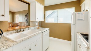 A kitchen with white cabinets, a granite countertop, a double sink, and a refrigerator with a paper on it. - Single Level Beachside Home, Great for Families & Dog Friendly - Walk to Beach (Galveston)