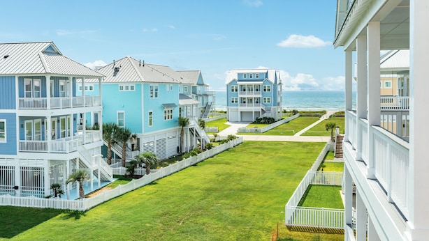 Una zona residencial costera con varias casas de dos pisos, con balcones y cercas blancas de piquete.