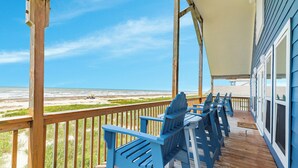 Eine Holzterrasse mit blauen Adirondack-Stühlen mit Blick auf einen Strand.