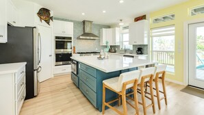Een moderne keuken met witte kasten, een groot eiland met barkrukken, een roestvrijstalen afzuigkap en uitzicht buiten.