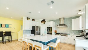Een moderne keuken met witte kasten, een groot eiland met barstoelen, een visdecoratie en een behangetje als spatwand.