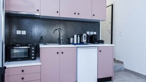 Cozinha compacta com armários cor-de-rosa, micro-ondas embutido, lava-louças e máquina de café.