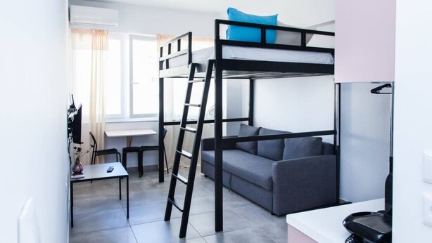 Quarto compacto e moderno com beliches, um sofá, uma mesa pequena e uma escrivaninha.