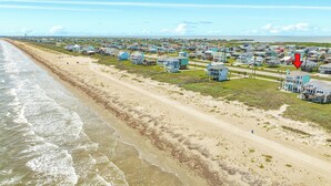 A coastal town with beachfront properties, a sandy beach, and a road running parallel to the shore. - Beachfront Pet Friendly Home w/ HOT TUB, Fenced Yard - Steps from Gulf & Beach (Galveston)