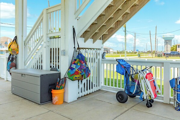 A covered porch with a white railing, a gray storage unit, and a colorful bag hanging on the railing.