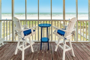 A wooden deck with two white Adirondack chairs and a small round table, overlooking a beach. - Updated Beachfront Home w/ Panoramic Gulf Views, Open Plan - Steps from Sand (Galveston)