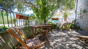 Un patio al aire libre con mesas y sillas de madera, rodeado de muros de piedra y follaje.