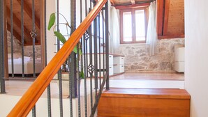 Una escalera de madera con barandilla de metal que lleva a una habitación con pared de piedra y una ventana con cortinas.