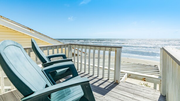 A wooden deck with chairs overlooking a beach.