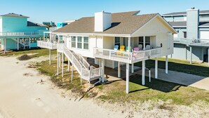 A beachfront house with a balcony, a staircase, and a view of the beach.