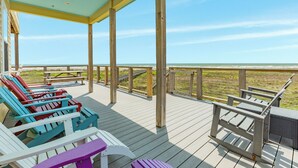 A wooden deck with Adirondack chairs and a picnic table, overlooking a beach.