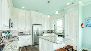 A kitchen with white cabinets, a granite countertop, a stainless steel refrigerator, and wooden stools.