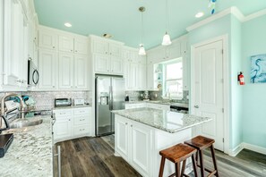A kitchen with white cabinets, a granite countertop, a stainless steel refrigerator, and wooden stools.
