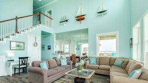 A spacious living room with a staircase, two sofas, a coffee table, and nautical decor.