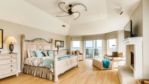 A spacious bedroom with a large bed, a sitting area with a fireplace, and a balcony with a view. - Beachfront Beauty w/ 2 Decks, No Bunk Beds, Open Plan & 220V NEMA 14-50 Charger (Galveston)