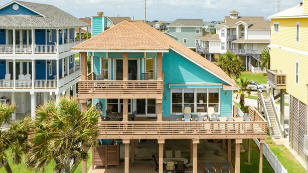 A two-story house with a balcony, a covered patio, and a fenced yard. - Beachfront Beauty w/ 2 Decks, No Bunk Beds, Open Plan & 220V NEMA 14-50 Charger (Galveston)