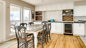 A kitchen with white cabinets, a wooden dining table with four chairs, and a large window. - Beachfront Beauty w/ 2 Decks, No Bunk Beds, Open Plan & 220V NEMA 14-50 Charger (Galveston)