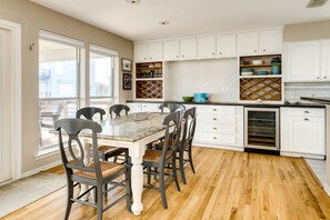 A kitchen with white cabinets, a wooden dining table with four chairs, and a large window.