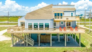 Una casa sulla spiaggia a due piani con un balcone, posti a sedere all'aperto e un patio coperto.