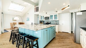 Un'ampia cucina con una grande isola, sgabelli da bar in legno e un soffitto alto con lucernari.