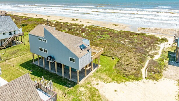 Una casa sulla spiaggia su due piani, con un balcone, un patio coperto e vista sull'oceano.