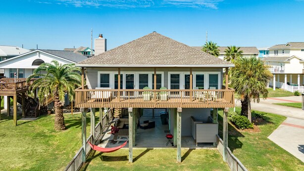 A two-story house with a covered patio, a hammock, and a small deck. - Cozy Beachside Home - Pet Friendly, Fenced Yard, Covered Deck, 0.5 blk to Beach (Galveston)