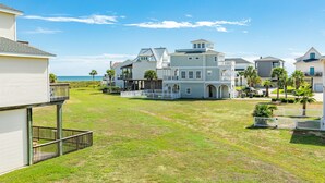 A beachfront property with multiple buildings, a grassy lawn, and a view of the ocean. - Cozy Beachside Home - Pet Friendly, Fenced Yard, Covered Deck, 0.5 blk to Beach (Galveston)