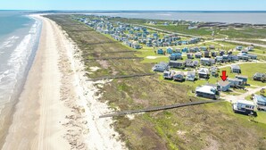 Ett flygbildsbild av ett bostadsområde vid kusten med hus, en strand och en bro.