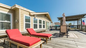 Une terrasse en bois avec deux chaises longues rouges et un espace salon abrité.