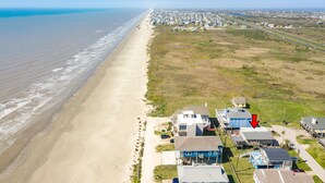 Une zone résidentielle côtière avec des maisons situées près de la plage, un ciel dégagé et une autoroute visible au loin.