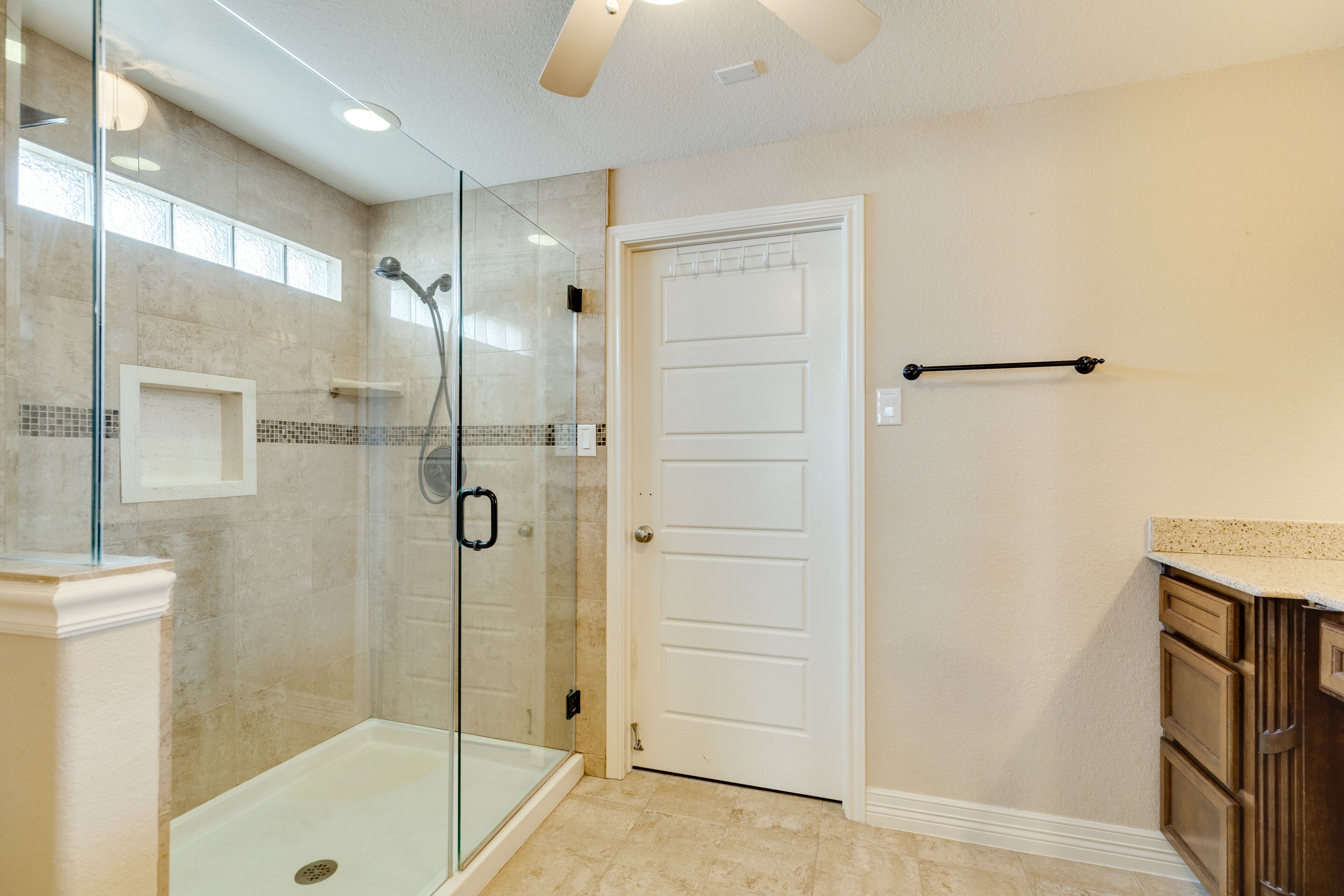 A modern bathroom with a glass-enclosed shower, a white door, and a countertop with cabinets.
