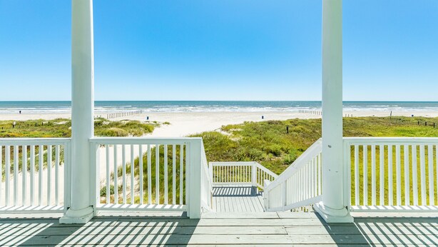 Une terrasse en bois avec des balustrades blanches donnant sur une plage.