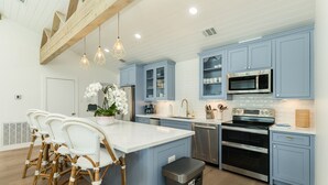 Una cocina moderna con armarios azules, electrodomésticos de acero inoxidable y una isla central con taburetes de bar.