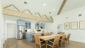Una cocina moderna con vigas de madera, una zona de comedor con mesa y sillas de madera, y armarios en color azul claro.