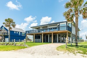 A beachfront property with a two-story structure, a covered outdoor seating area, and a sandy pathway leading to the entrance. - Updated Beachfront Home - Open Plan, 4 King+Bunks, Across from Walkover (Galveston)